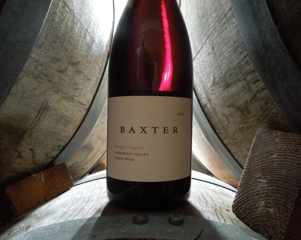A bottle of Baxter Langley Vineyard Anderson Valley Pinot Noir standing on oak barrels in the cellar.