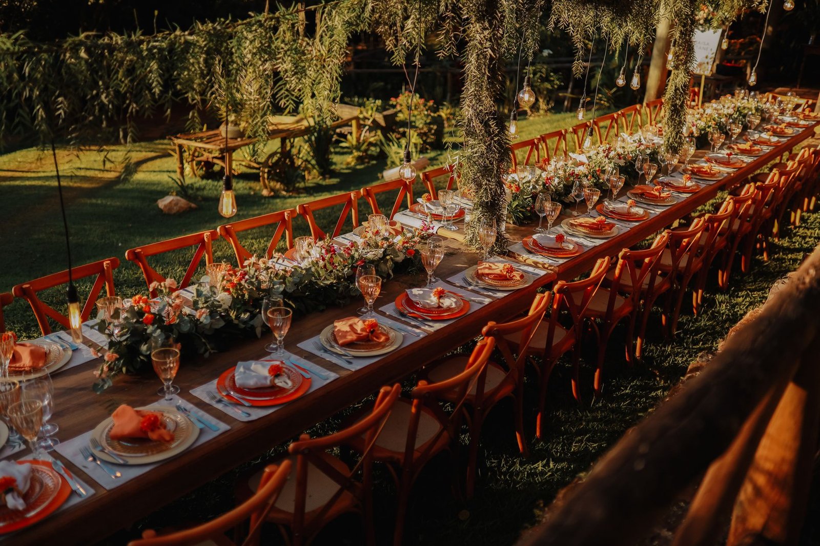 A long table set under trees and lit for an evening dinner
